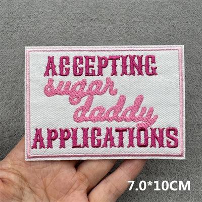 Embroidered patch with pink text on a gray background