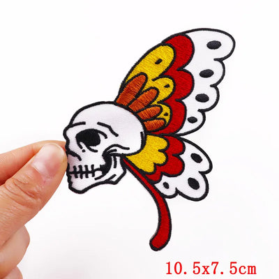 Butterfly-shaped patch with skull design held by a hand, on a white background.