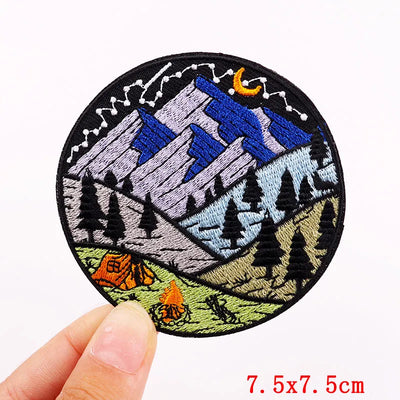 Circular embroidered patch with mountain and camping design held by a hand, size 7.5x7.5cm.