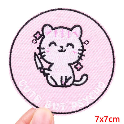 Circular patch with a cartoon cat design on a pink background, held by a hand.