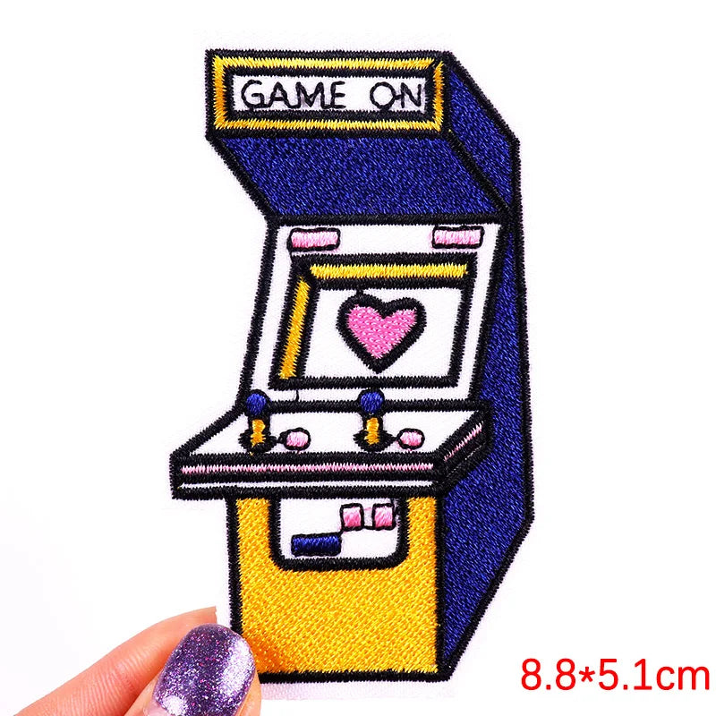Embroidered patch of an arcade machine with a heart on the screen, held by a hand.