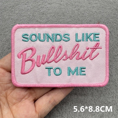 Embroidered patch with text held by a hand on a gray background