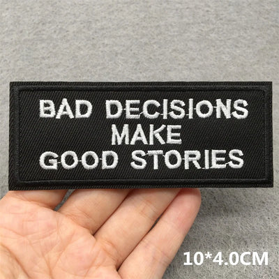 Embroidered patch with 'Bad decisions make good stories' text held by a hand on a gray background.