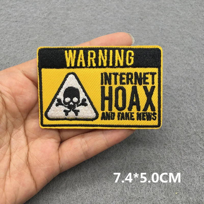 Patch with 'WARNING: INTERNET HOAX AND FAKE NEWS' text held in a hand on a gray background