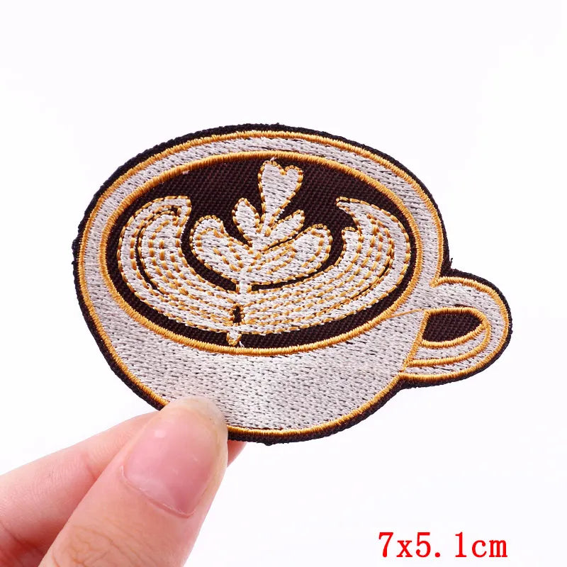 Embroidered patch of a coffee cup with a starbucks logo held by a hand on a white background.