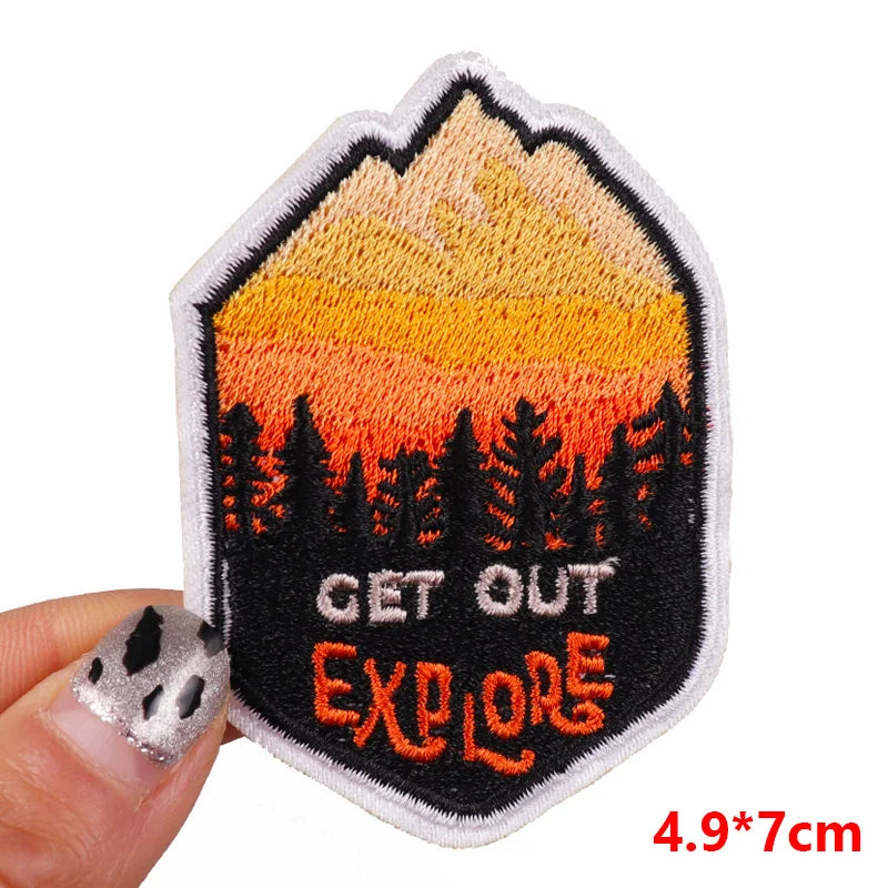 Embroidered patch with mountain and trees design, featuring 'GET OUT EXPLORE' text, held by a hand.