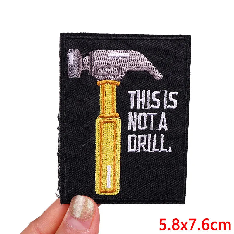 Embroidered patch with a hammer and 'THIS IS NOT A DRILL' text held by a hand.