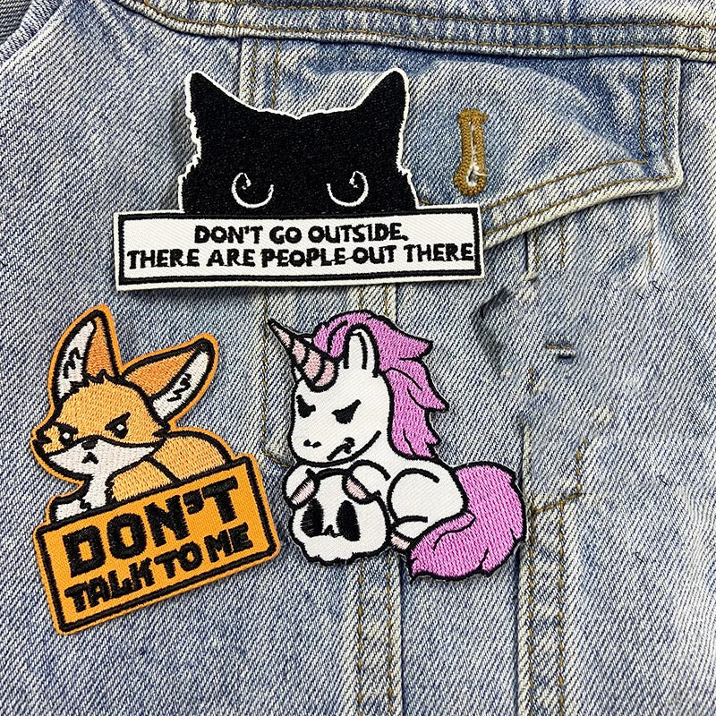 Three patches on a denim jacket: a black cat, a fox, and a unicorn with text.