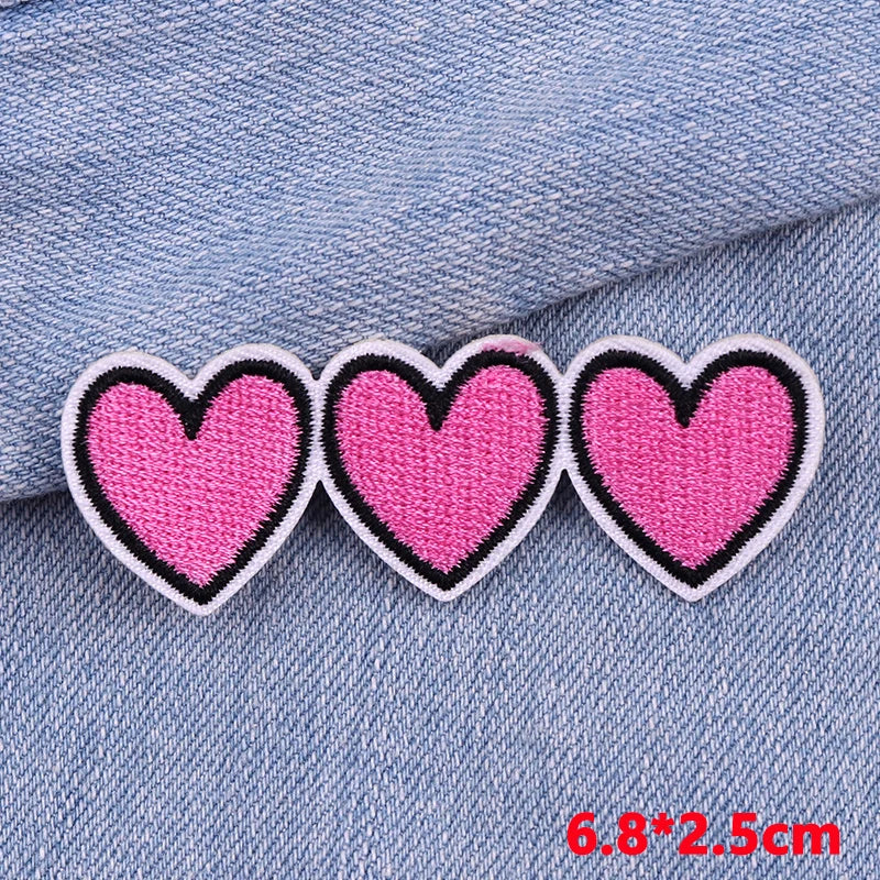 Three pink heart-shaped patches with black borders on a denim background.
