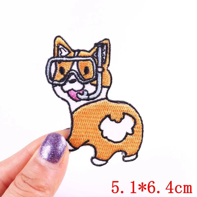 Embroidered patch of a dog with goggles held by a hand on a white background