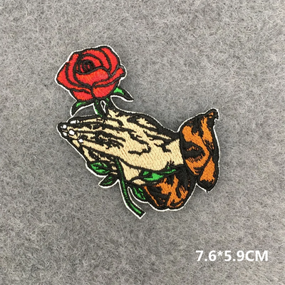 Embroidered patch of a hand holding a rose and a butterfly on a gray background