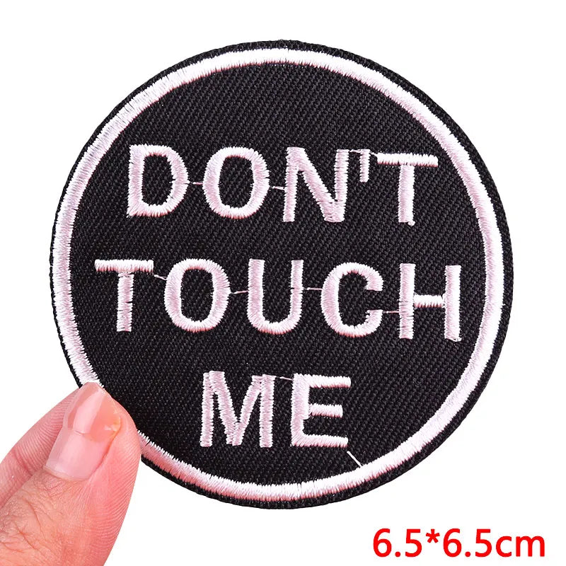 Round patch with 'DON'T TOUCH ME' text held by a hand on a white background