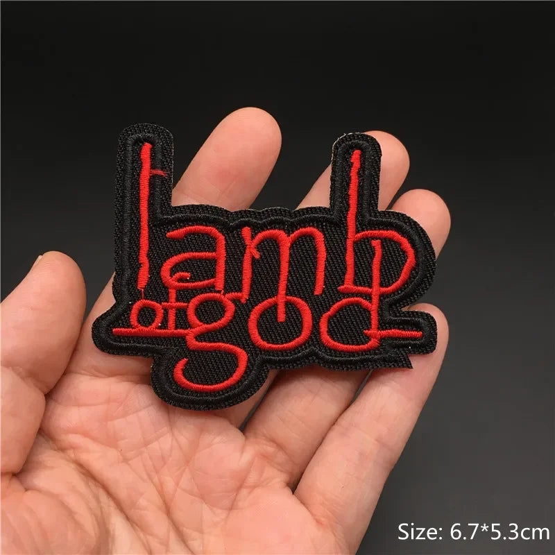 Hand holding a black and red Lamb of God embroidered iron-on patch 6.7x5.3cm on a dark background