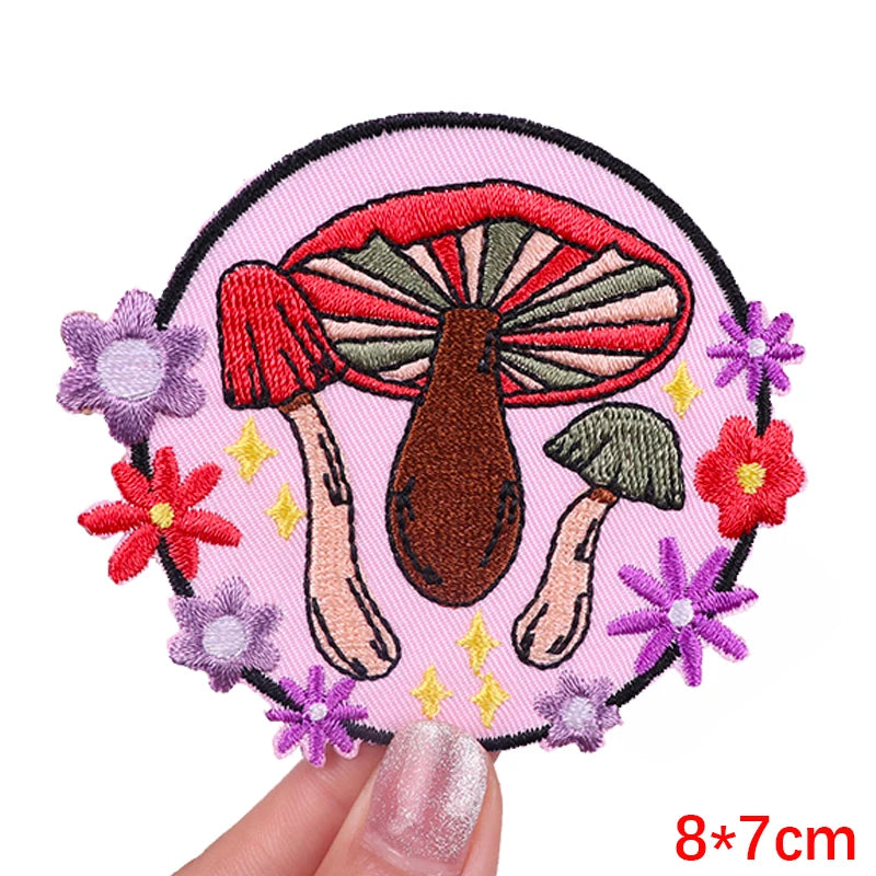 Embroidered patch with mushrooms and flowers held by a hand on a white background