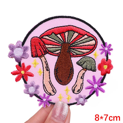 Embroidered patch with mushrooms and flowers held by a hand on a white background