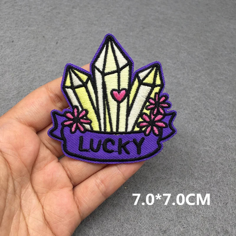 Embroidered patch with crystals and 'LUCKY' text held in a hand on a gray background
