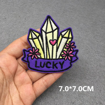 Embroidered patch with crystals and 'LUCKY' text held in a hand on a gray background