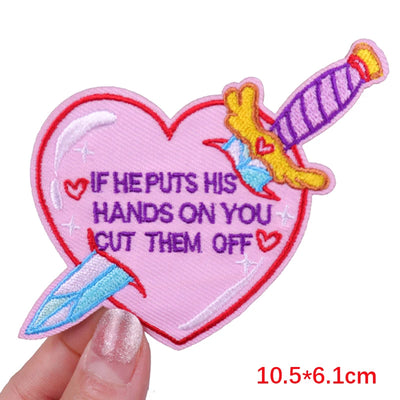 Heart-shaped patch with a sword design and text held by a hand on a white background