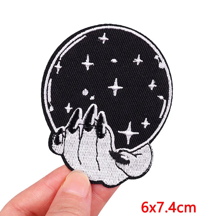 Embroidered patch of a hand holding a moon with stars, held by a hand against a white background.