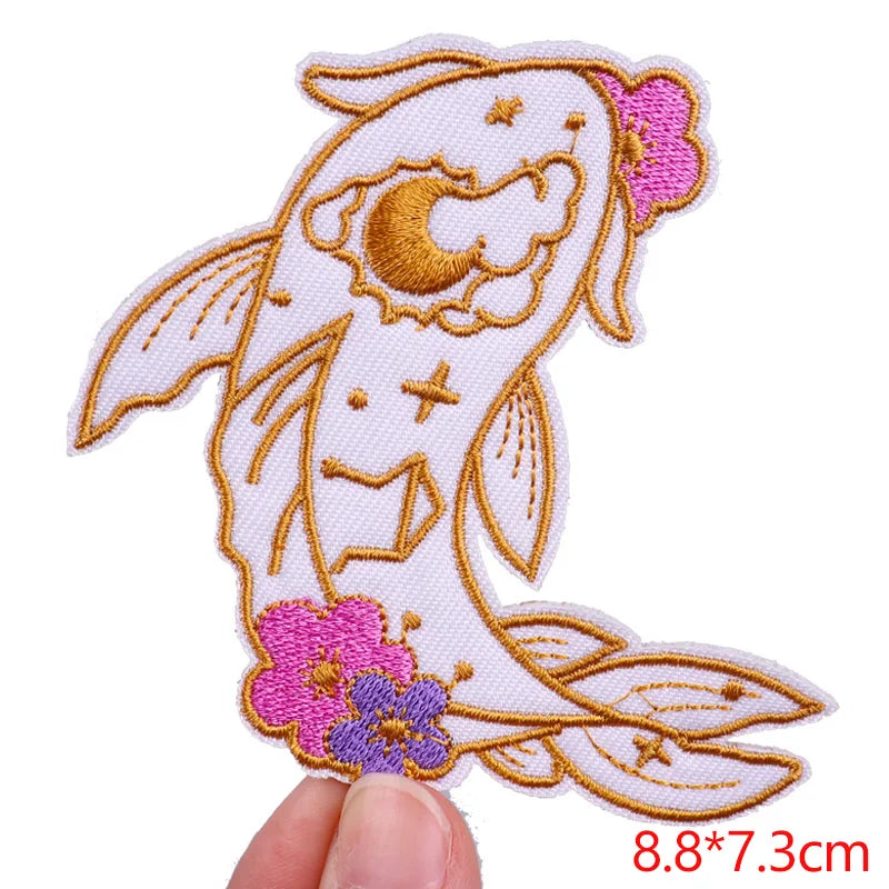 Embroidered patch of a fish with flowers held by a hand on a white background
