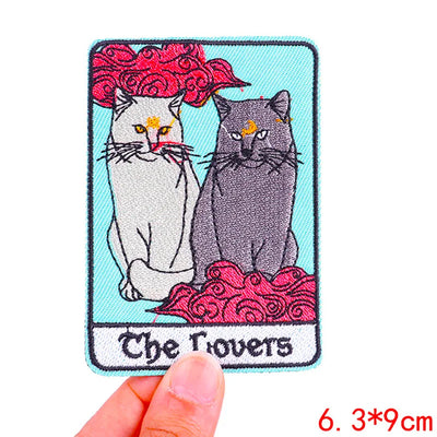 Embroidered patch with two cats and 'The Lovers' text, held by a hand.