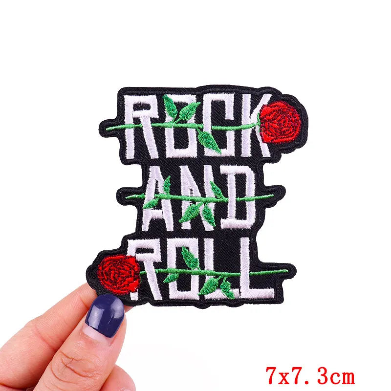 Embroidered patch with 'Rock and Roll' text and roses held by a hand on a white background