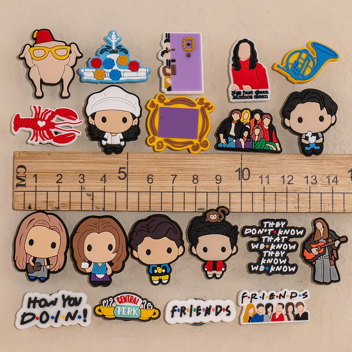 Collection of Friends-themed Shoe charms on a beige background with wooden ruler for scaling