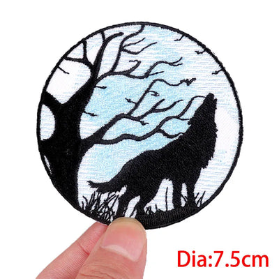 Round patch with a wolf howling at the moon design held by a hand, with a white background.