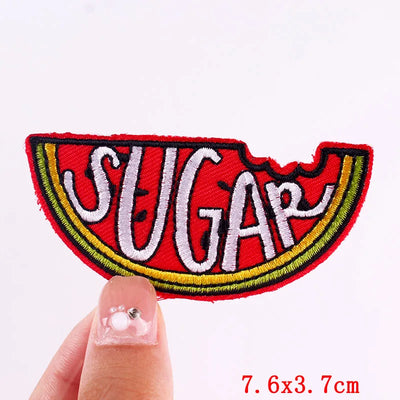 Embroidered patch with 'SUGAR' text held by a finger on a white background