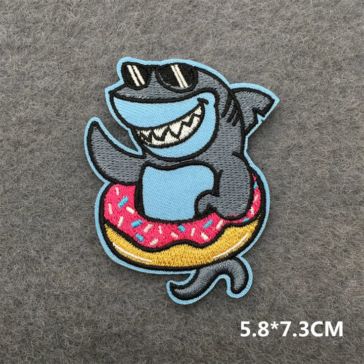 Embroidered patch of a shark with sunglasses and a donut on a gray background