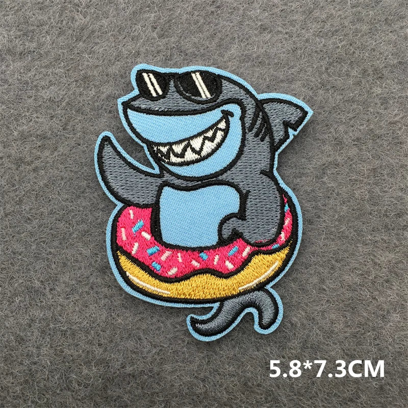 Embroidered patch of a shark with sunglasses and a donut on a gray background