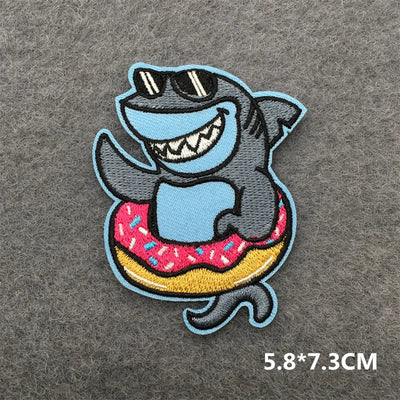 Embroidered patch of a shark with sunglasses and a donut on a gray background