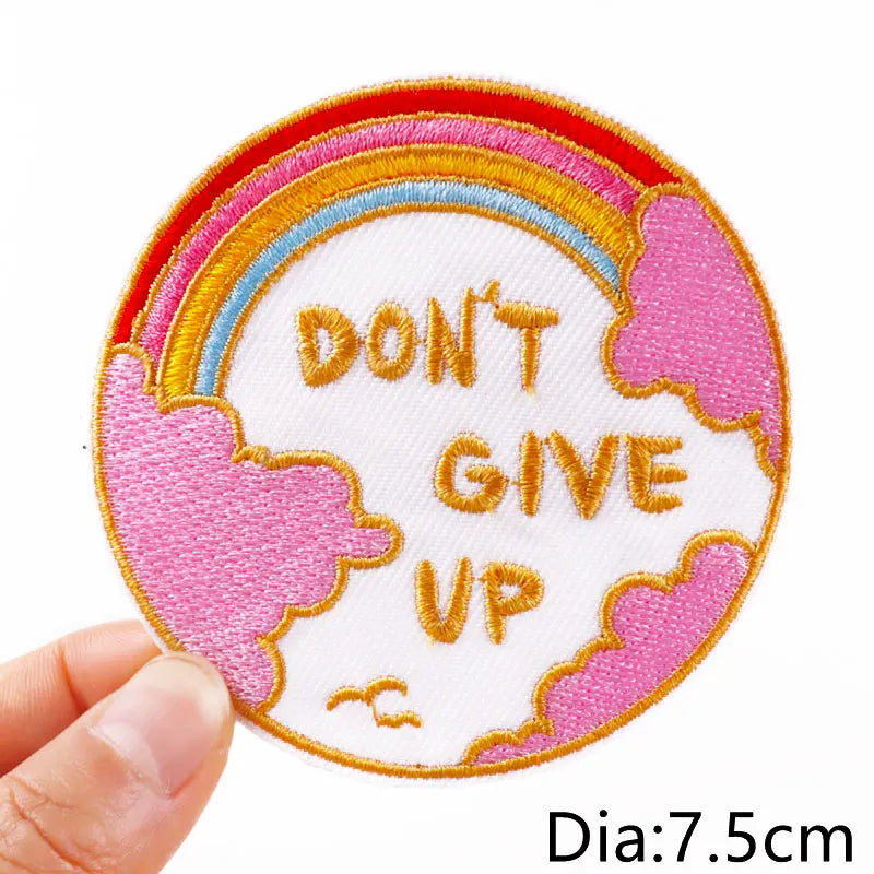 Circular patch with 'Don't Give Up' text held by a hand, against a white background