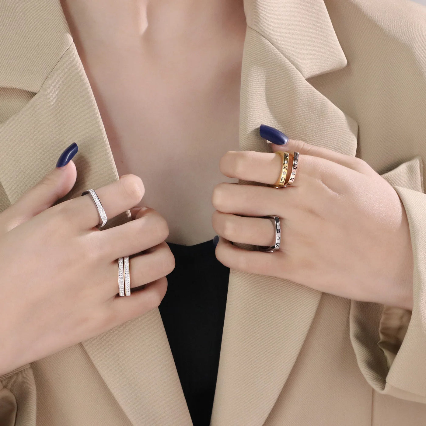 Two hands wearing multiple rings on a neutral background