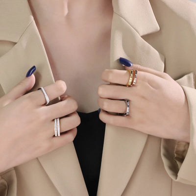 Two hands wearing multiple rings on a neutral background