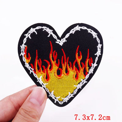 Heart-shaped patch with flames and barbed wire held by a hand on a white background