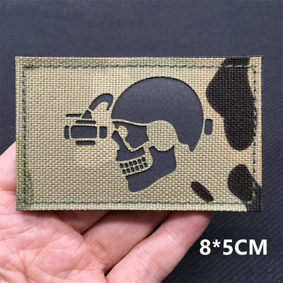 Tactical patch with skull and grenade design held in a hand against a dark background