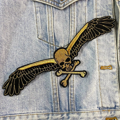 Denim jacket with a skull and crossbones patch featuring wings.