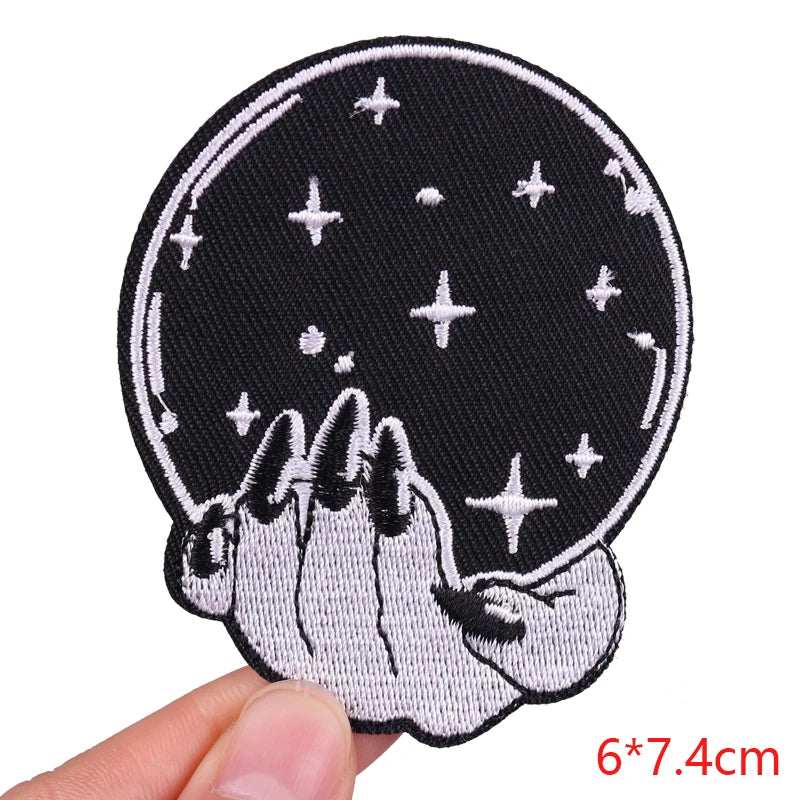 Embroidered patch with hands holding a crystal ball and stars, held by a hand against a white background.