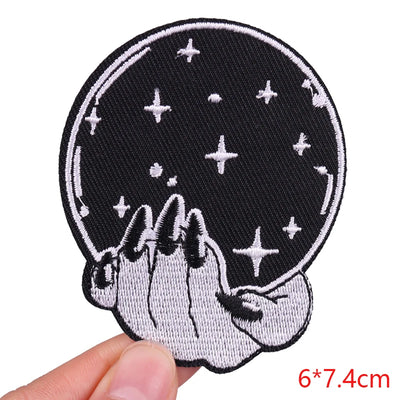 Embroidered patch with hands holding a crystal ball and stars, held by a hand against a white background.
