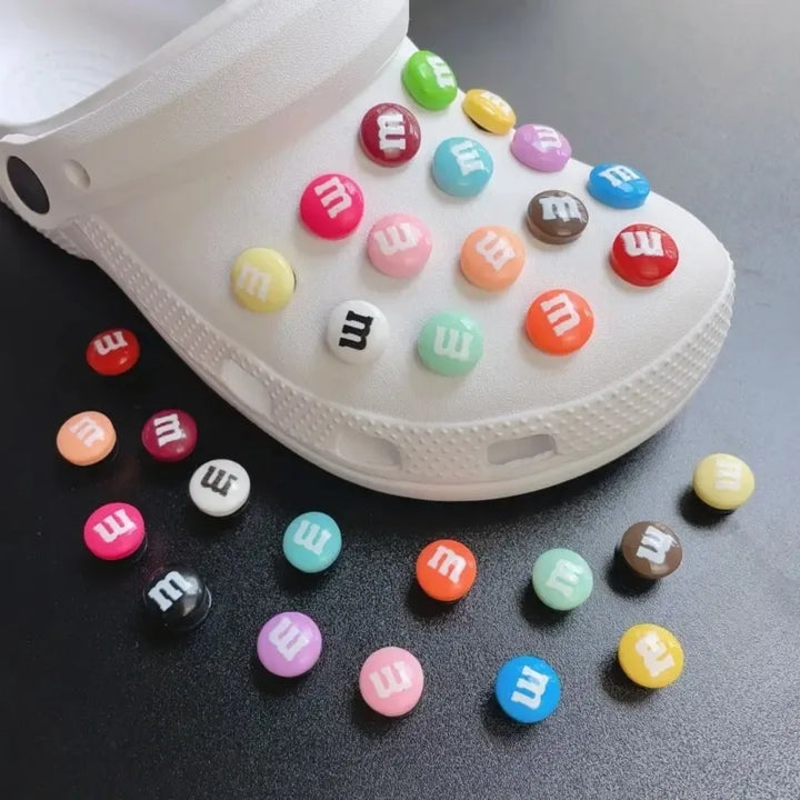 White clog shoe with colorful M&amp;M-themed buttons on a dark surface