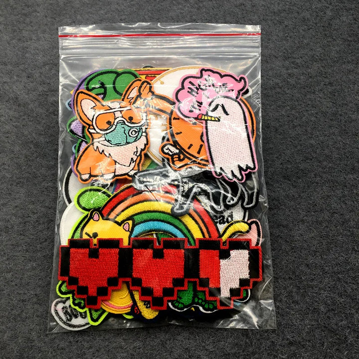 Colorful patches including a fox, ghost, and rainbow design in a clear plastic bag on a dark background.