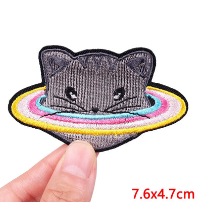Embroidered patch of a cat with a rainbow halo held by a hand, on a white background.