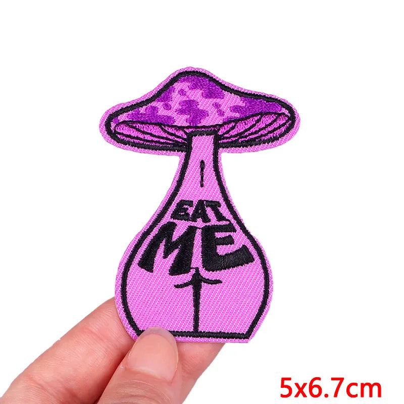 Purple mushroom patch with 'Eat Me' text held by a hand on a white background