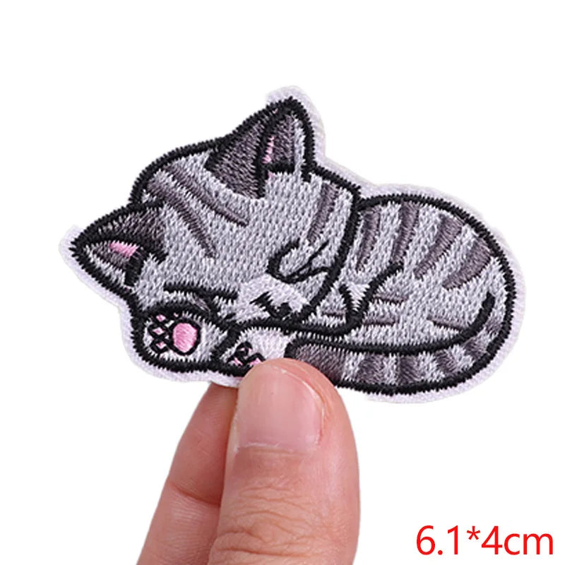 Embroidered patch of a cat held between fingers with dimensions displayed