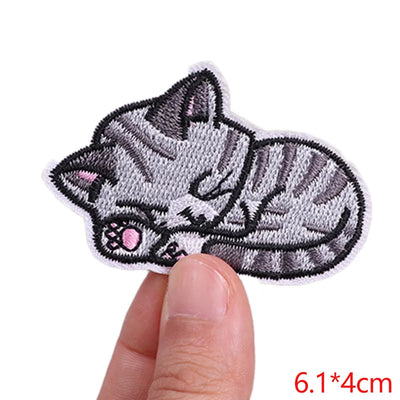 Embroidered patch of a cat held between fingers with dimensions displayed