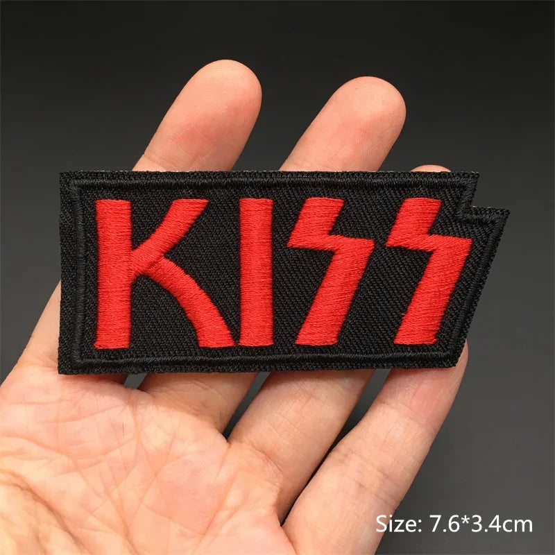 Hand holding a black and red Kiss embroidered iron-on patch 7.6x3.4cm on a dark background