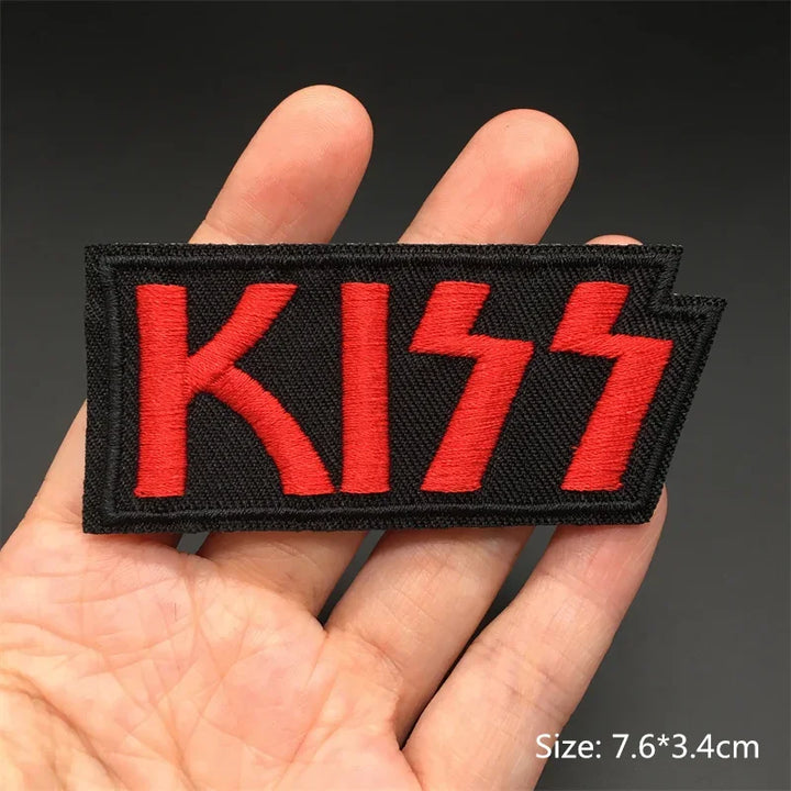 Hand holding a black and red Kiss embroidered iron-on patch 7.6x3.4cm on a dark background