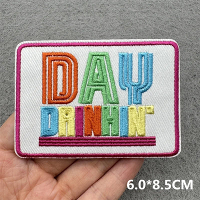 Embroidered patch with colorful text held in a hand on a gray background