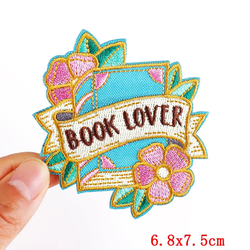 Embroidered patch with 'BOOK LOVER' text held by a hand, on a white background.